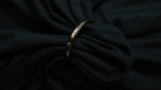 A gold-toned segmented bangle bracelet with black inlay details, shown resting on draped black fabric.
