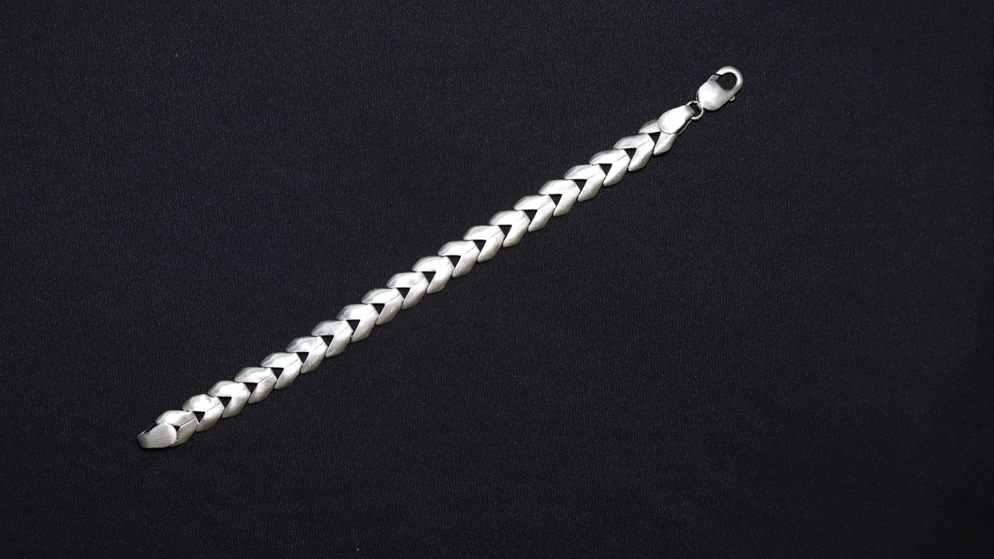 A silver-toned braided chain bracelet with a lobster clasp, displayed diagonally on a solid black background.