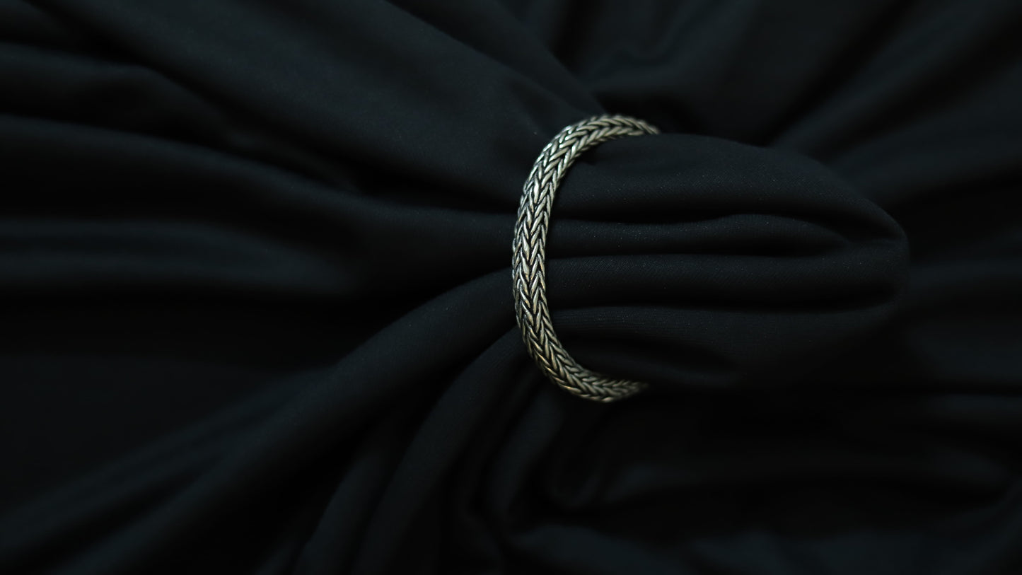 A silver braided ring or tie-back strap holding a black fabric bag or garment, shown in a close-up shot against a dark background.