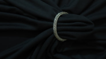 A silver braided ring or tie-back strap holding a black fabric bag or garment, shown in a close-up shot against a dark background.