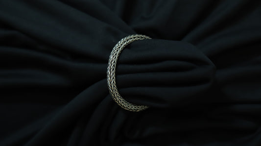 A silver braided rope bracelet or tie clip shown wrapped around a black fabric surface.