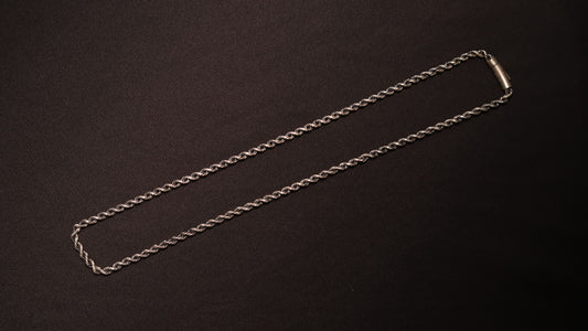 A silver-toned twisted rope chain necklace with a simple rectangular clasp, laid flat on a dark textured background.