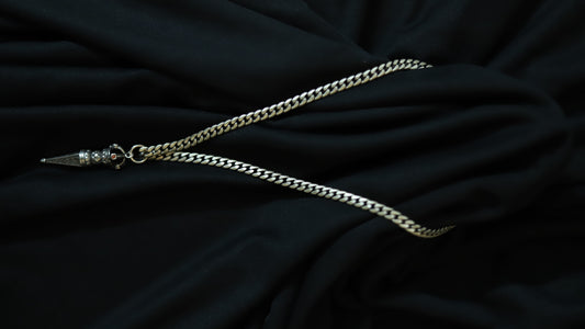 A silver-toned chain necklace with a decorative pointed pendant, laid out on draped black fabric.