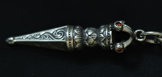 A silver-toned metal keychain charm featuring intricate engraved patterns, a decorative textured center, and two small red gemstone accents, shown on a black background.