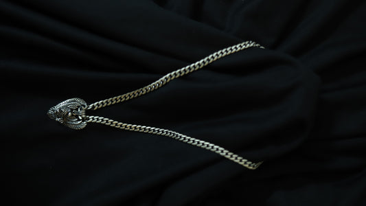A silver-toned chain necklace with a textured, decorative oval pendant, laid out on a draped black fabric background.
