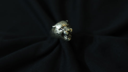 A silver-toned ring shaped like a roaring panther head, displayed on a dark black fabric background.