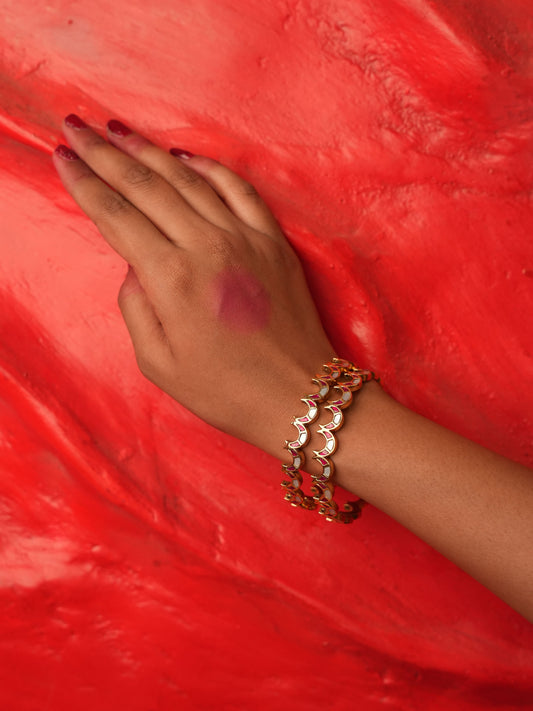 A close-up of a person's hand and wrist wearing a gold-toned multi-layered bangle bracelet, resting on a textured bright red surface.