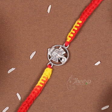 A red and yellow braided string bracelet with a silver-toned elephant charm, laid diagonally on a brown textured background with small white decorative elements.