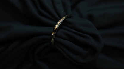 A gold-toned segmented bangle bracelet with black inlay details, shown resting on draped black fabric.