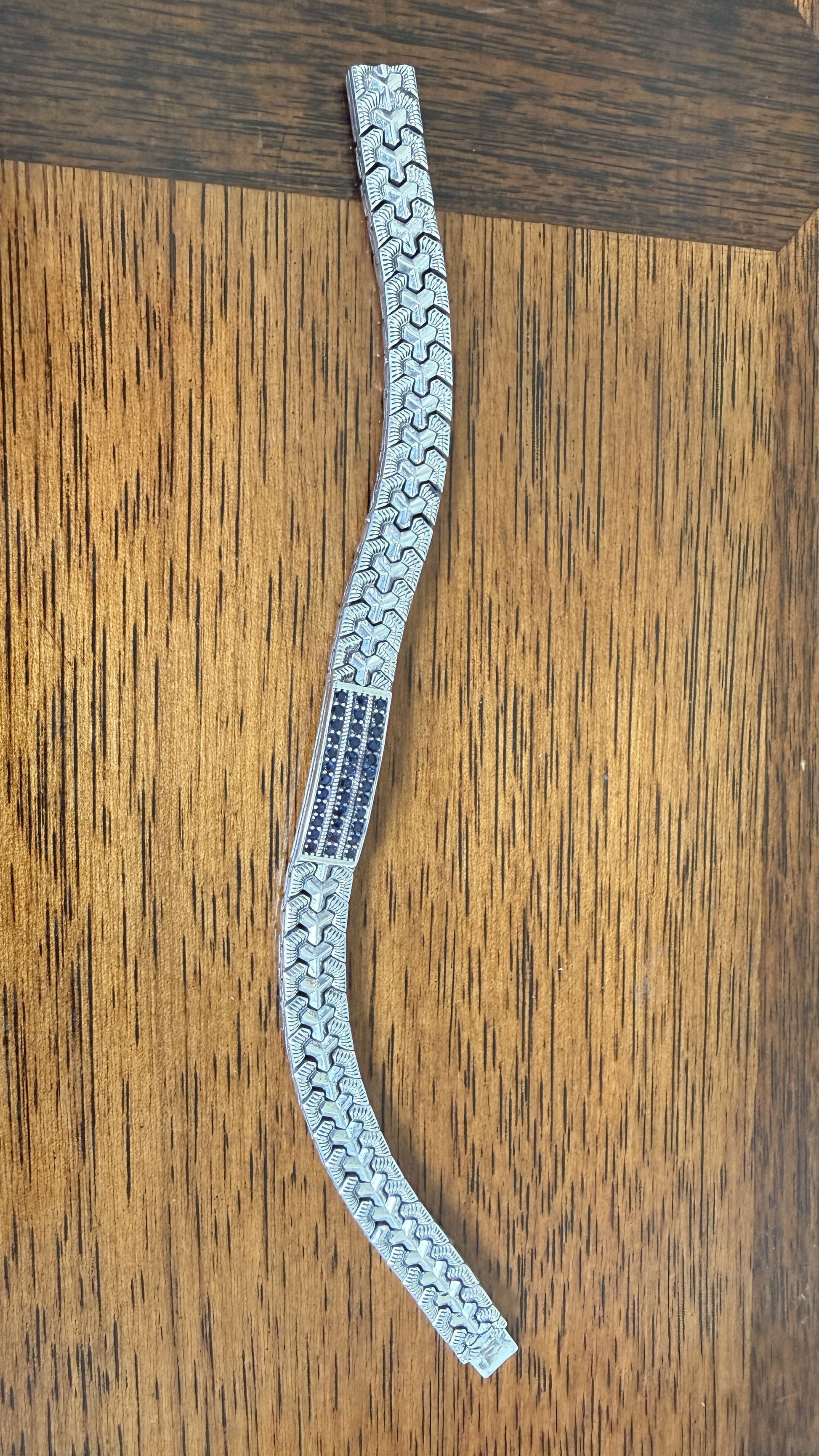 A silver-toned metal bracelet with a repeating wavy geometric pattern, displayed on a brown wooden surface.