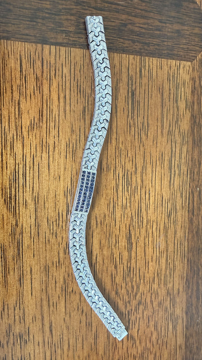 A silver-toned metal bracelet with a repeating wavy geometric pattern, displayed on a brown wooden surface.