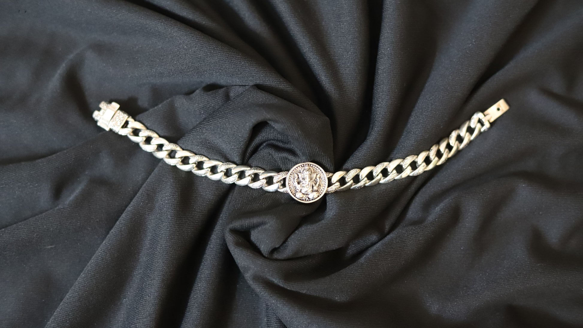 A silver-toned chain bracelet featuring a central circular medallion charm, laid flat on draped black fabric.