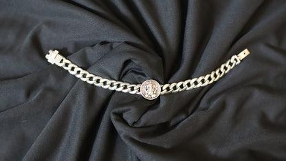 A silver-toned chain bracelet featuring a central circular medallion charm, laid flat on draped black fabric.