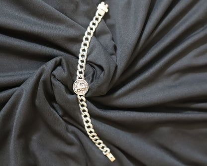 A silver-toned chain bracelet with a round bezel-set clear stone, displayed on a draped black fabric background.