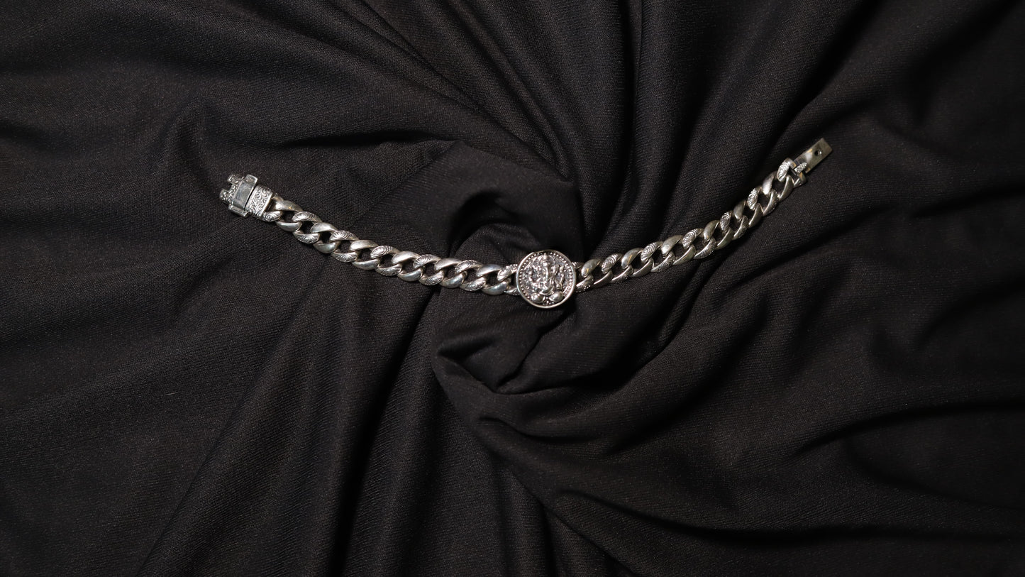 A silver-toned chain belt with a circular medallion buckle, displayed on a draped black fabric background.