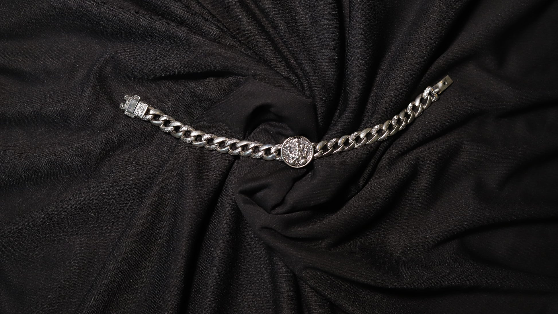A silver-toned chain belt with a circular medallion buckle, displayed on a draped black fabric background.