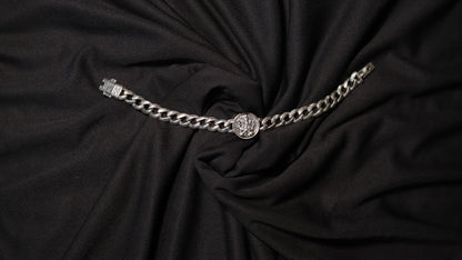 A silver-toned chain belt with a circular medallion buckle, displayed on a draped black fabric background.
