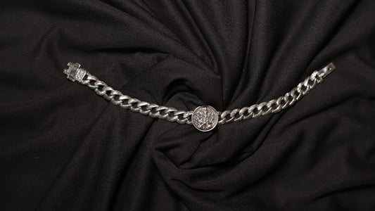 A silver-toned chain belt with a central round medallion and a clasp on the left, displayed on a draped black fabric background.