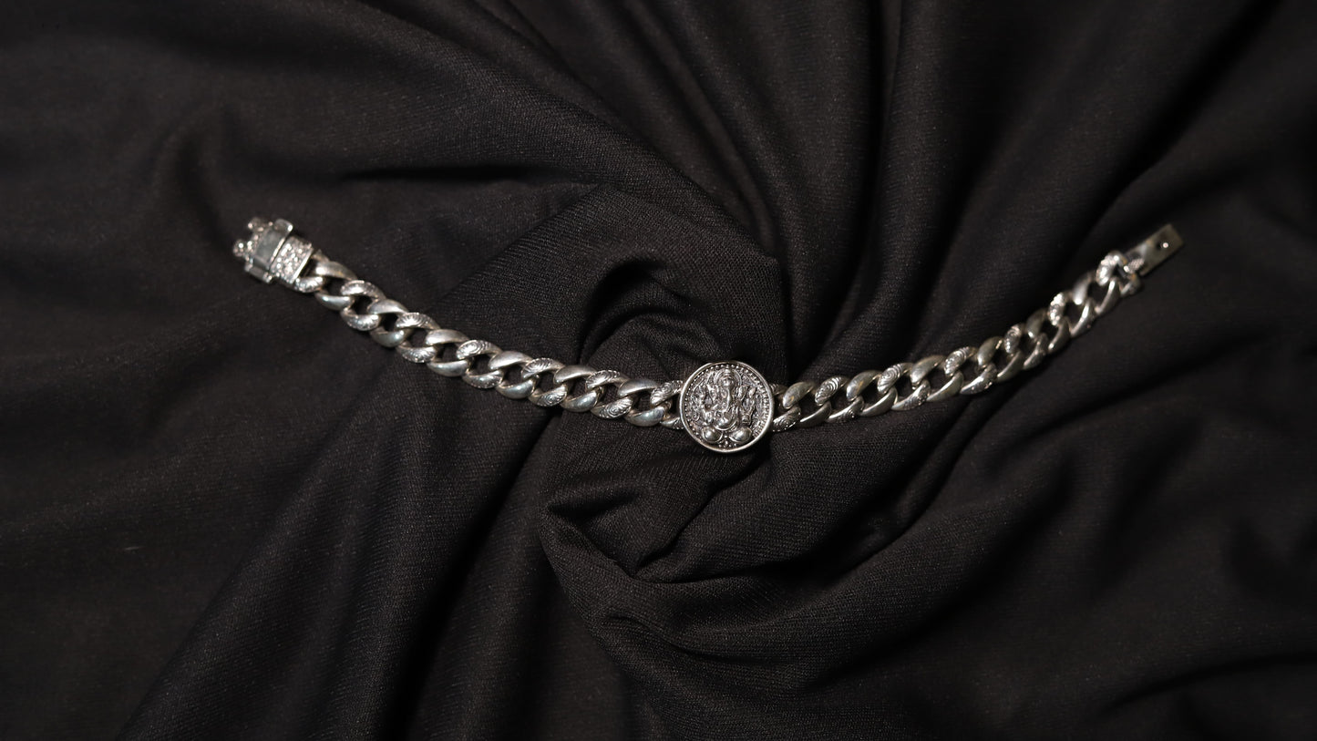 A silver chain belt with a central medallion and a buckle on the left, displayed on a draped black fabric background.