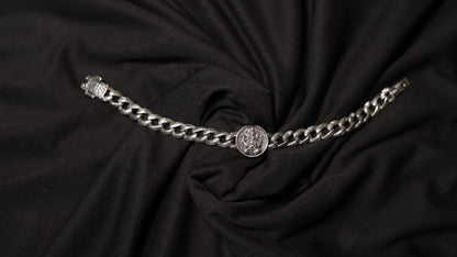 A silver chain belt with a central medallion and a buckle on the left, displayed on a draped black fabric background.