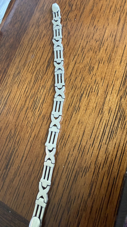 A single white decorative chain link bracelet with geometric and scroll-like links, laid diagonally on a brown wooden surface.