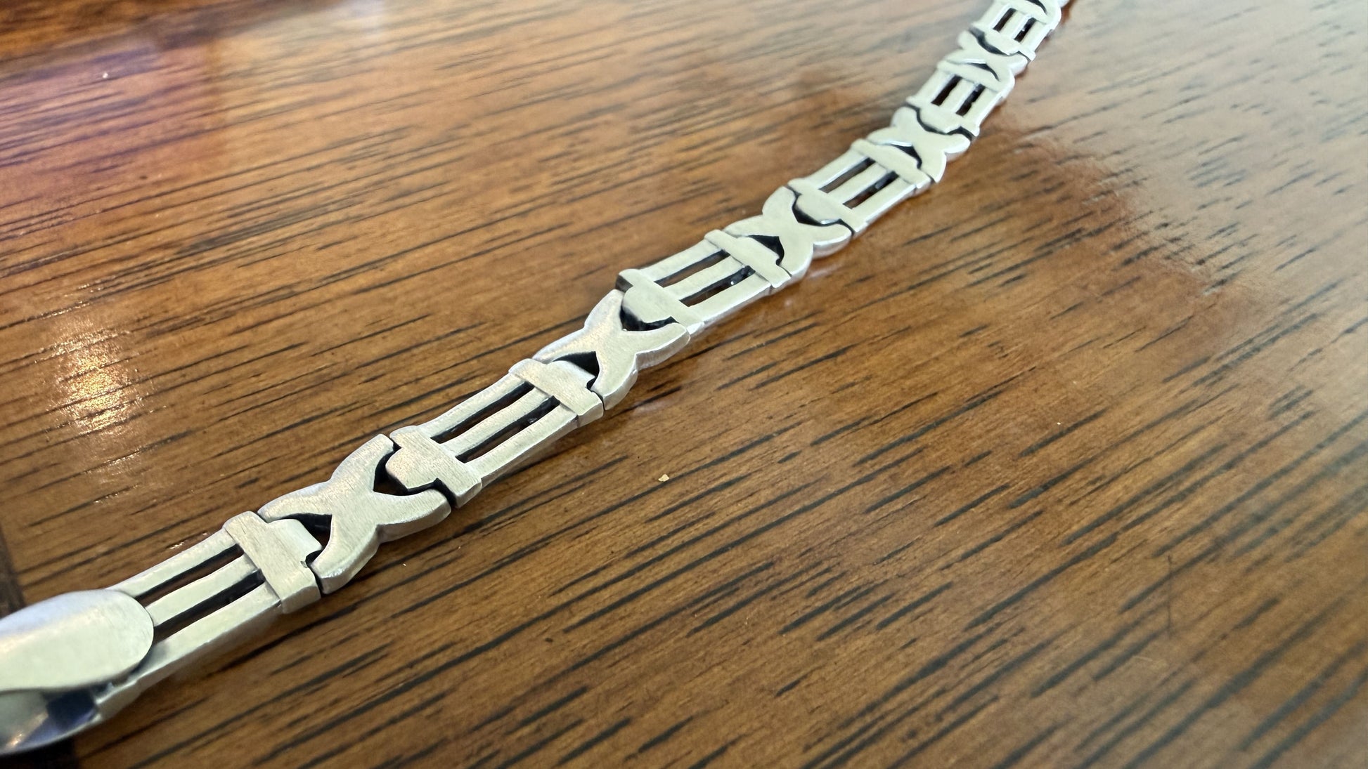 A close-up of a silver-toned metal link chain bracelet resting on a polished wooden tabletop.