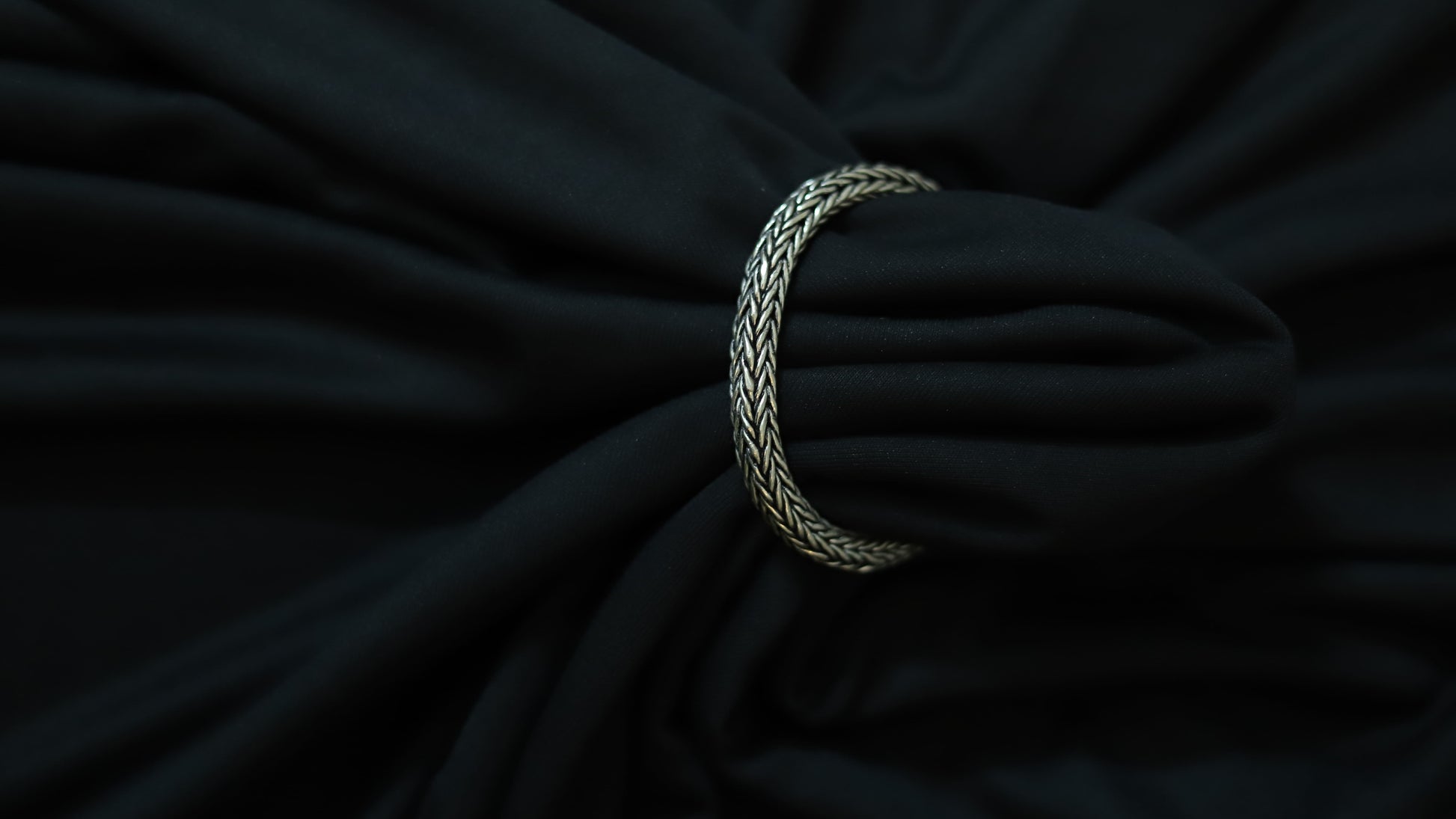 A silver braided ring or tie-back strap holding a black fabric bag or garment, shown in a close-up shot against a dark background.