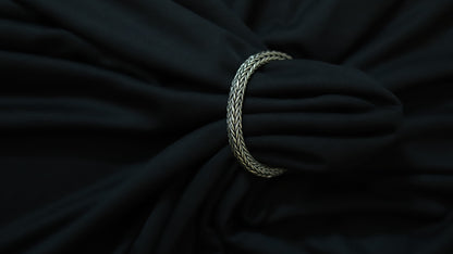 A silver braided ring or tie-back strap holding a black fabric bag or garment, shown in a close-up shot against a dark background.