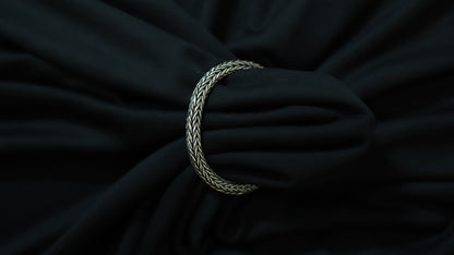 A silver braided rope bracelet or tie clip shown wrapped around a black fabric surface.