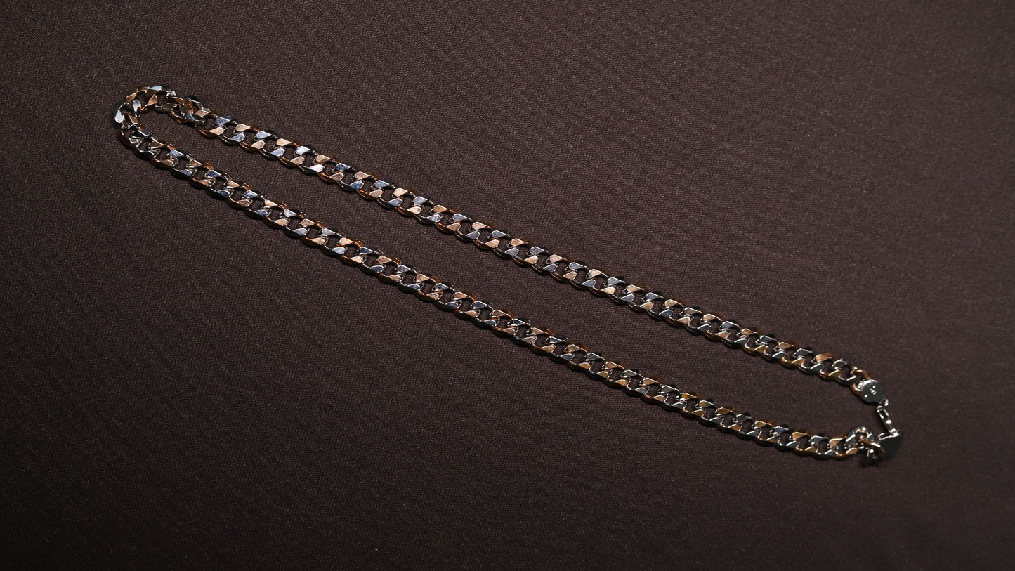 A silver-toned metal curb chain necklace laid out diagonally on a dark brown textured background.