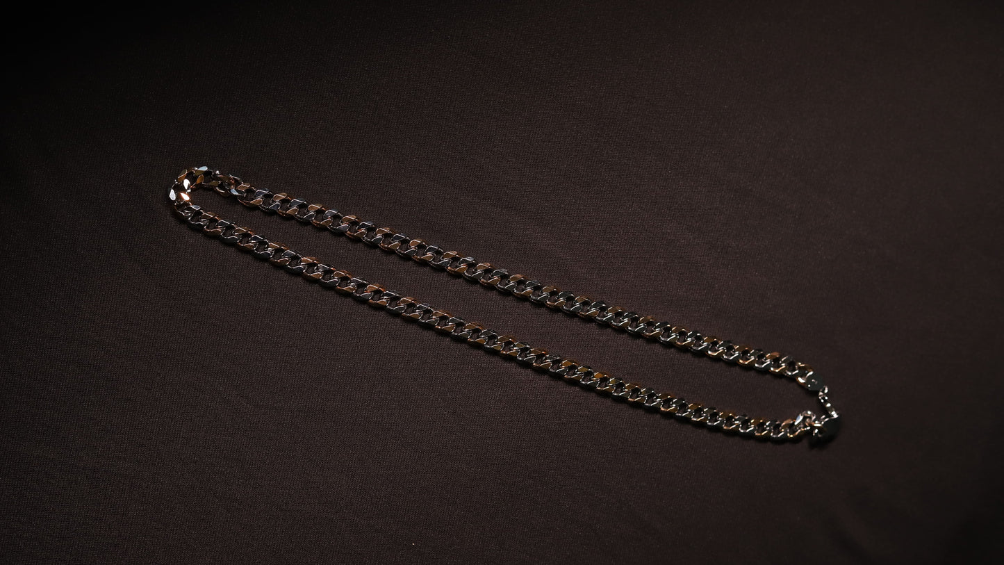A silver-toned metal chain necklace laid out in a curved shape on a dark, textured background.