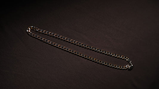 A silver-toned metal chain necklace laid out in a curved shape on a dark, textured background.