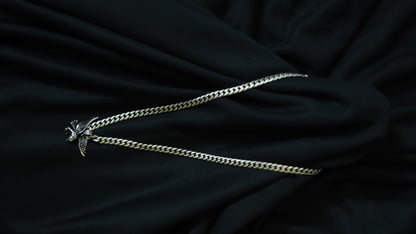 A silver-toned metal chain necklace with a small winged bird pendant, laid out on a draped black fabric background.
