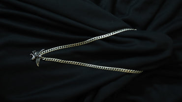 A silver-toned curb chain necklace with a small bird pendant, laid out on draped black fabric.