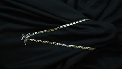 A silver-toned curb chain necklace with a small bird pendant, laid out on draped black fabric.