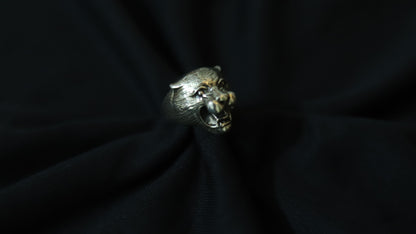 A silver-toned ring shaped like a roaring panther head, displayed on a dark black fabric background.