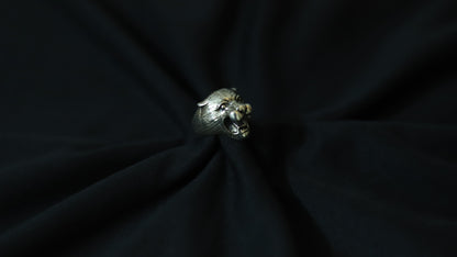 A silver-toned ring shaped like a lion's head, resting on a dark black fabric background.