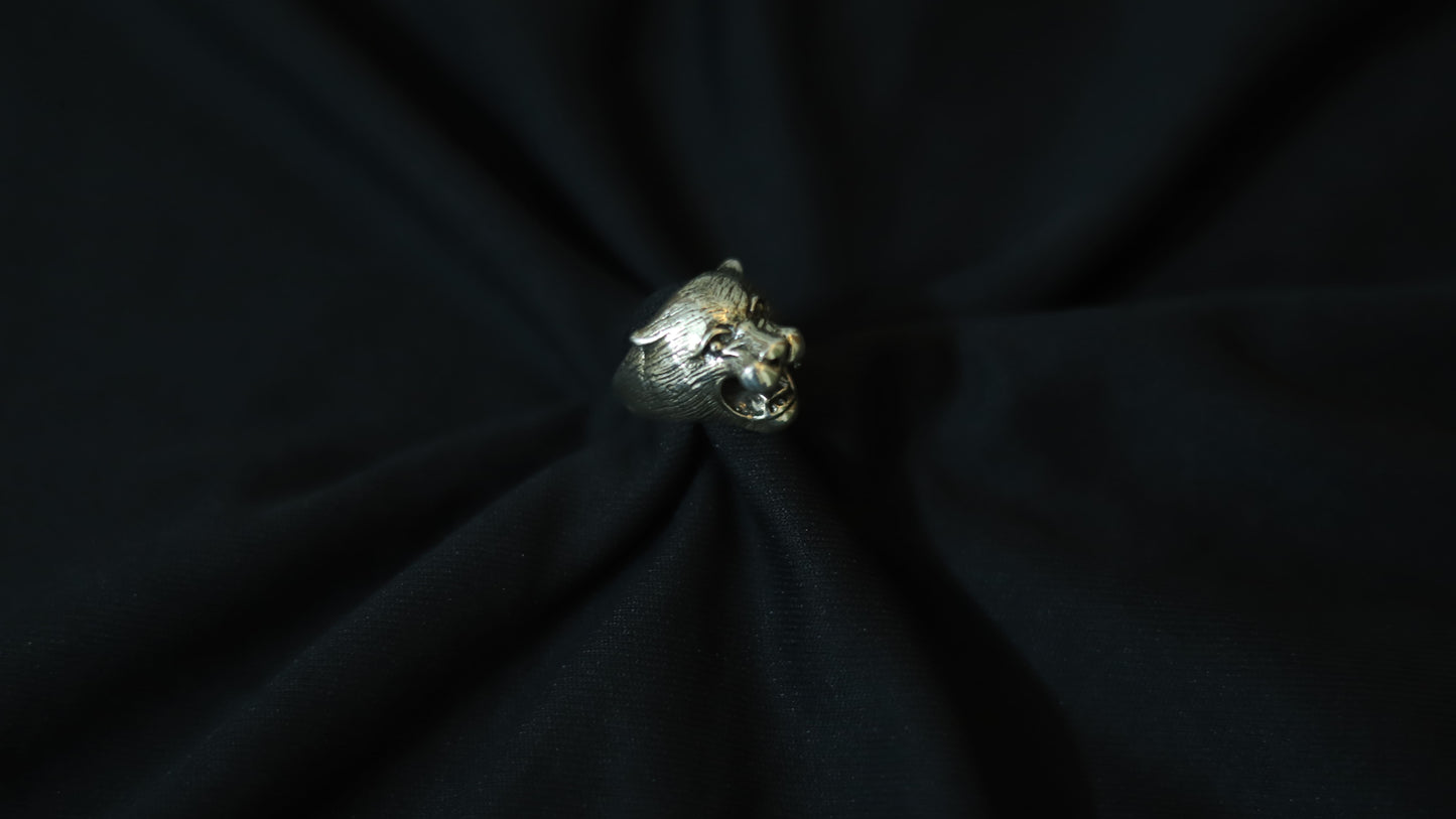 A silver-toned metallic ring shaped like a stylized animal head, displayed on a black fabric background.