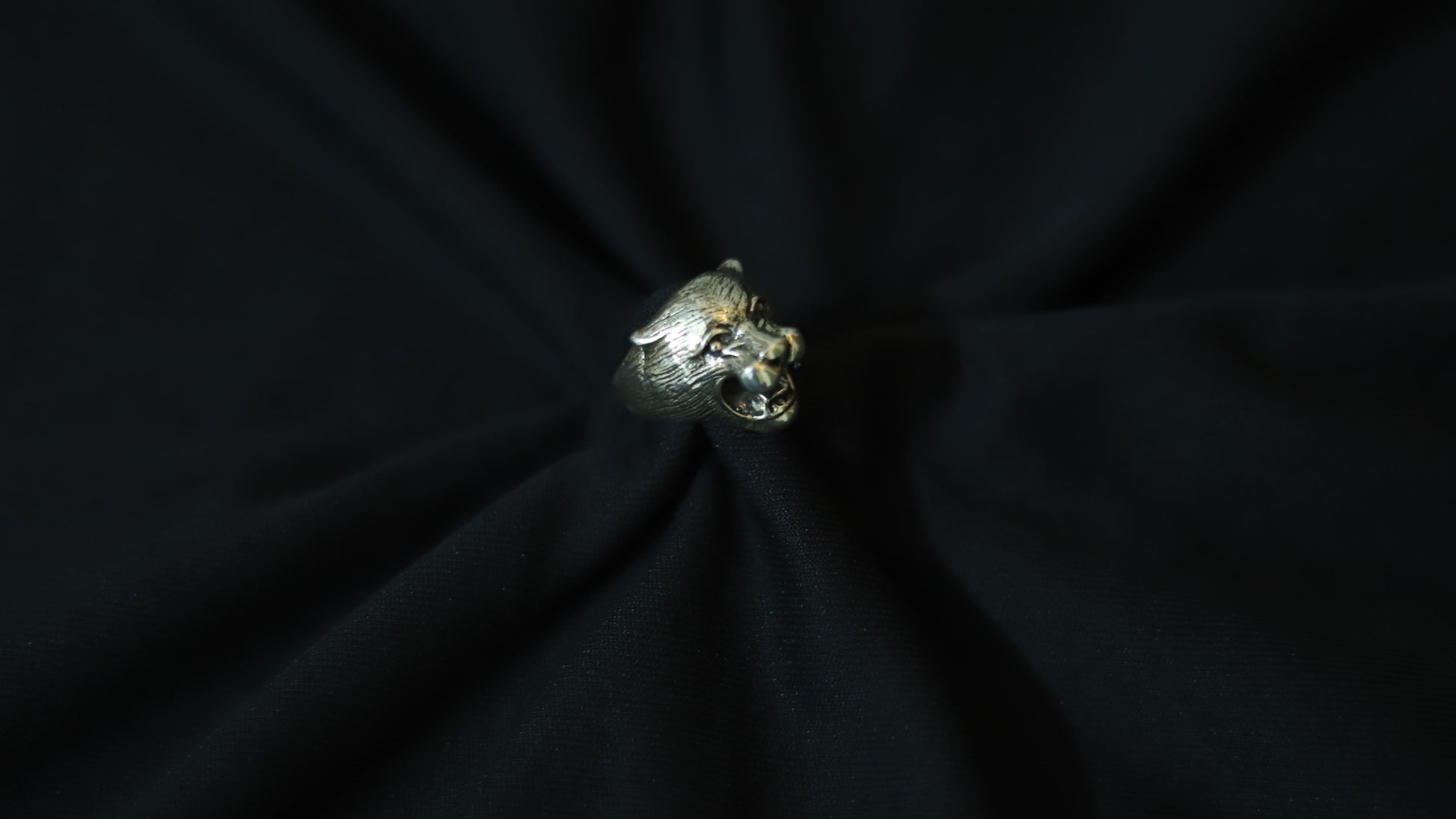 A silver-toned metallic ring shaped like a stylized animal head, displayed on a black fabric background.