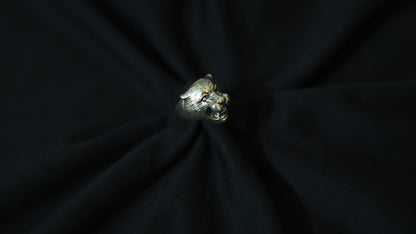 A silver-toned metallic ring shaped like a stylized animal head, displayed on a black fabric background.