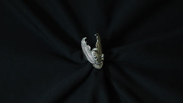 A silver-toned metal ring shaped like a stylized eagle or bird head with wings, centered on a dark black fabric background.