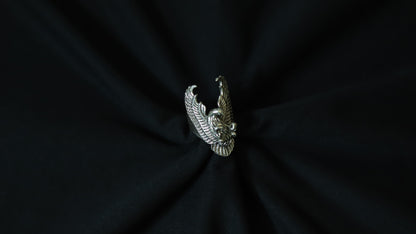 A silver-toned metal ring shaped like a stylized eagle or bird head with wings, centered on a dark black fabric background.