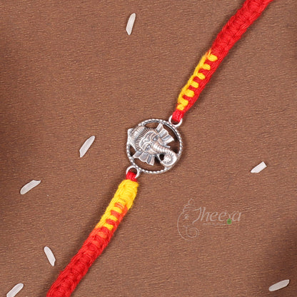 A red and yellow braided string bracelet with a silver-toned elephant charm, laid diagonally on a brown textured background with small white decorative elements.